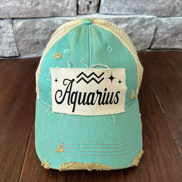 Mint green cap with 'Aquarius' patch on a wooden surface and stone wall background