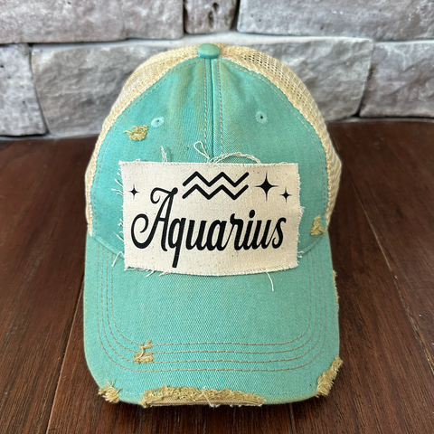 Mint green cap with 'Aquarius' patch on a wooden surface and stone wall background