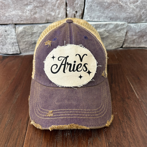 Distressed baseball cap with 'Aries' patch on a wooden surface and stone wall background