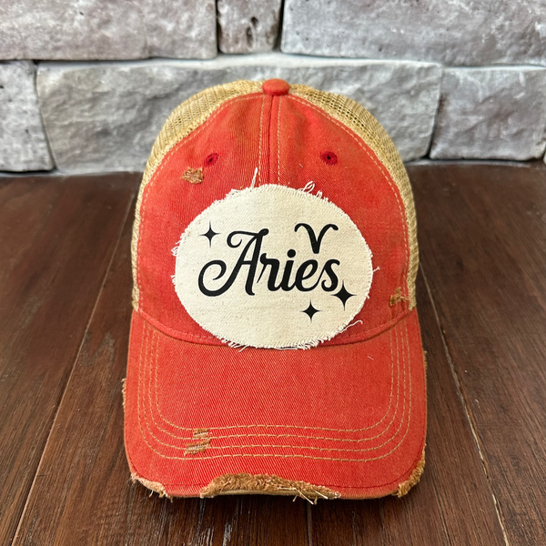 Red cap with 'Aries' patch on a wooden surface and stone wall background