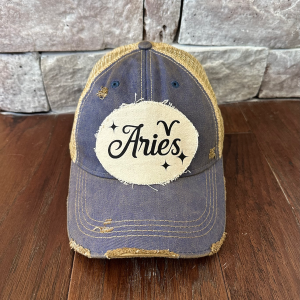 Blue cap with 'Aries' patch on a wooden surface and stone wall background