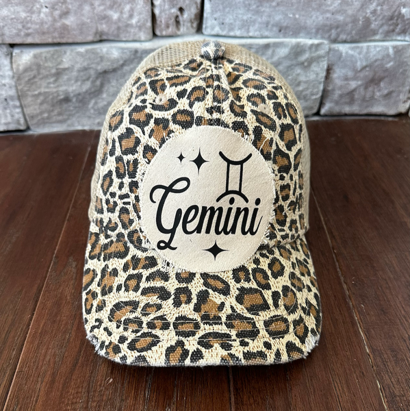 Leopard print cap with 'Gemini' logo on a wooden surface and stone wall background