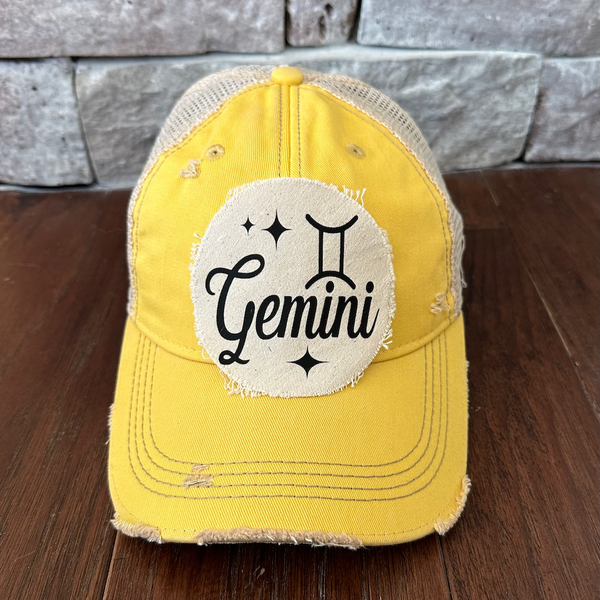 Yellow cap with 'Gemini' patch on a wooden surface and stone wall background