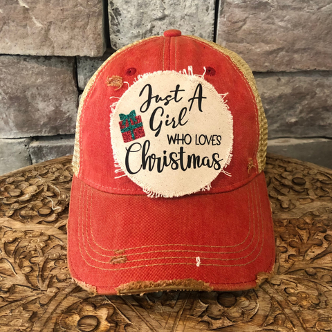 Red cap with a patch that says 'Just A Girl Who Loves Christmas' on a wooden surface.