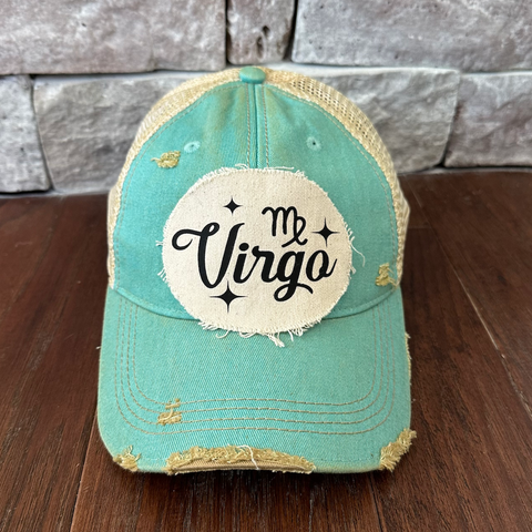 Teal cap with 'Virgo' patch on a wooden surface and stone wall background