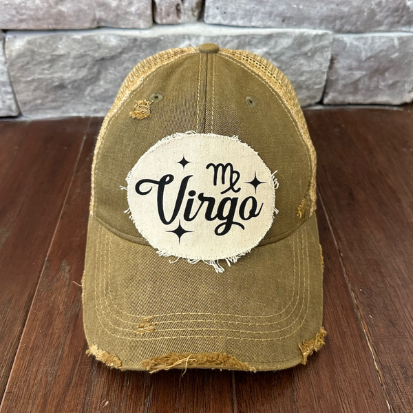 Olive green cap with 'My Virgo' patch on a wooden surface with stone wall background