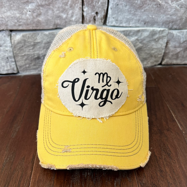 Yellow cap with 'My Virgo' patch on a wooden surface and stone wall background