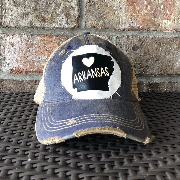 Arkansas hat by BohoGroove with black Arkansas state graphic and white heart on a distressed off-white custom patch on a navy vintage distressed snapback trucker hat.