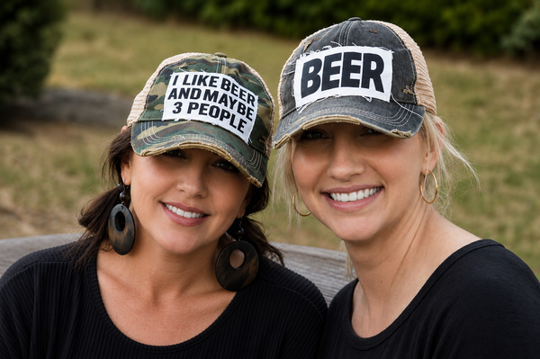 Two women wearing BohoGroove funny drinking hats on vintage distressed snapback caps outdoors.