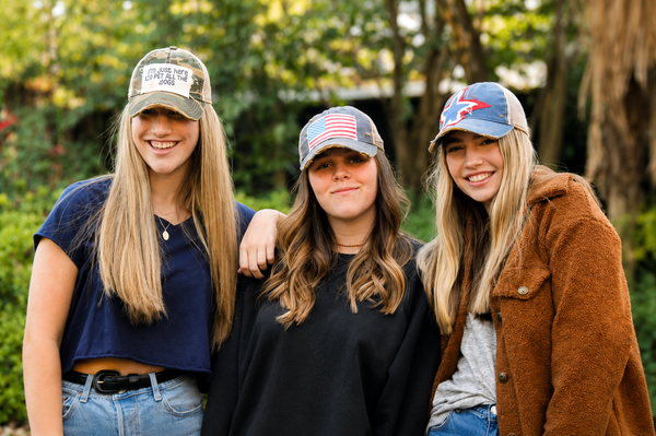 Three women modeling BohoGroove vintage distressed snapback hats with dog lover, American flag, and patriotic patch designs.