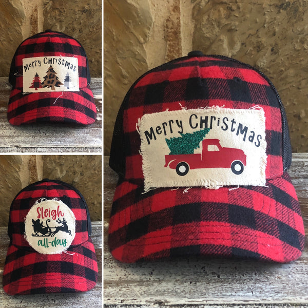 Buffalo plaid Christmas hat collection by BohoGroove featuring Merry Christmas truck, Merry Christmas trees, and Sleigh All Day designs on red and black buffalo plaid snapback trucker hats with distressed off-white patches.
