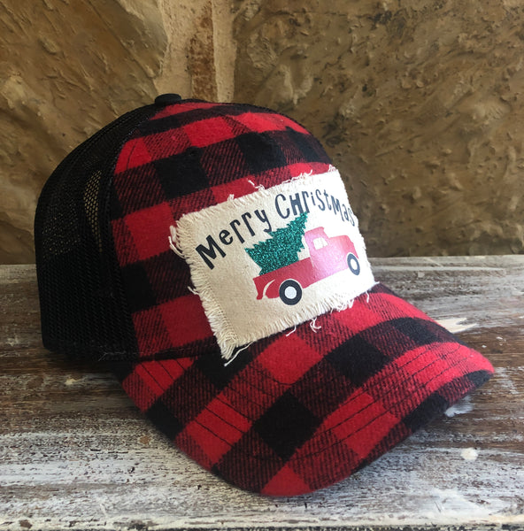 Buffalo Plaid Christmas Truck hat by BohoGroove with black Merry Christmas lettering, a red vintage pickup truck carrying a green Christmas tree, and distressed off-white patch on a red and black buffalo plaid snapback trucker hat left side.