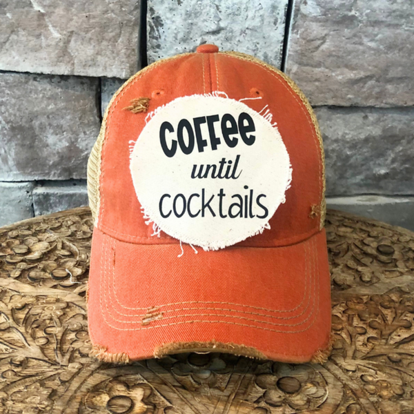 Orange cap with a white patch reading 'Coffee until cocktails' against a stone wall background