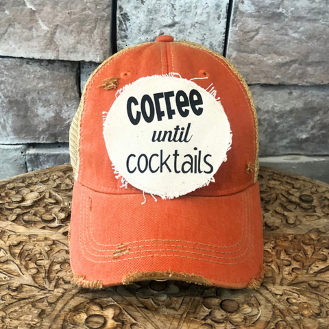 Orange cap with a white patch reading 'Coffee until cocktails' against a stone wall background