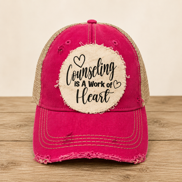Counseling Is A Work of Heart hat by BohoGroove with black script lettering and heart graphics on a distressed off-white patch on a pink vintage distressed snapback trucker hat.