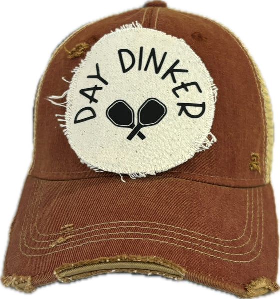 Day Dinker hat by BohoGroove featuring black Day Dinker lettering and crossed pickleball paddles graphic on a distressed off-white patch on a brick red vintage distressed snapback trucker hat.