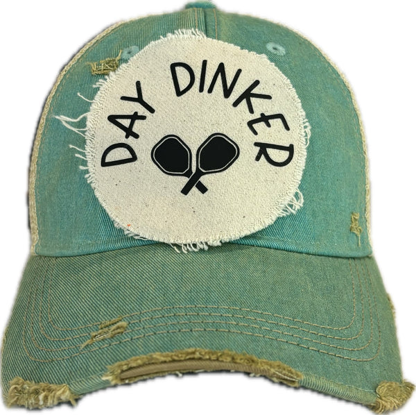 Day Dinker hat by BohoGroove featuring black Day Dinker lettering and crossed pickleball paddles graphic on a distressed off-white patch on an ocean blue vintage distressed snapback trucker hat.