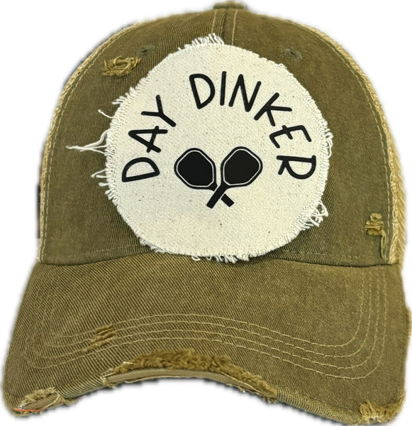 Day Dinker hat by BohoGroove featuring black Day Dinker lettering and crossed pickleball paddles graphic on a distressed off-white patch on an olive vintage distressed snapback trucker hat.