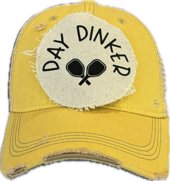 Day Dinker hat by BohoGroove featuring black Day Dinker lettering and crossed pickleball paddles graphic on a distressed off-white patch on a yellow vintage distressed snapback trucker hat.