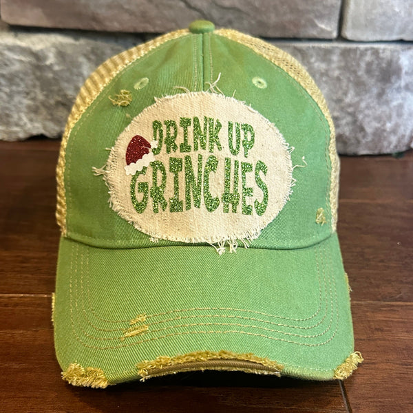 Drink Up Grinches hat by BohoGroove with glitter green Drink Up Grinches lettering and a red Santa hat graphic on a distressed off-white custom patch on a mint vintage distressed snapback.