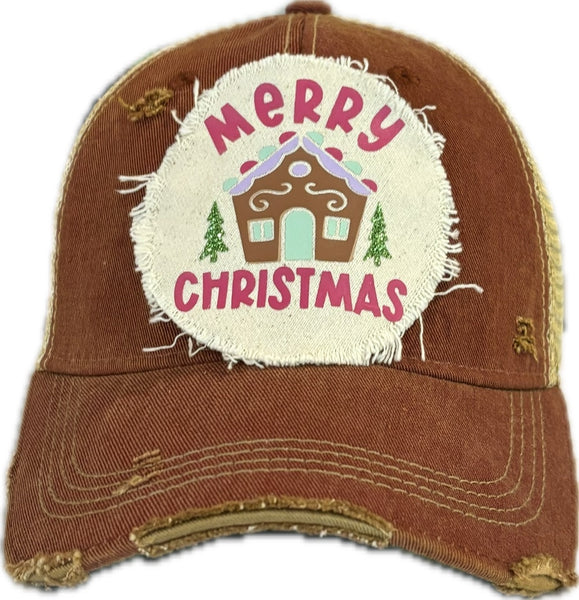 Gingerbread House hat by BohoGroove with pink Merry Christmas lettering, a gingerbread house graphic, and green trees on a distressed off-white patch on a brick red vintage distressed snapback.