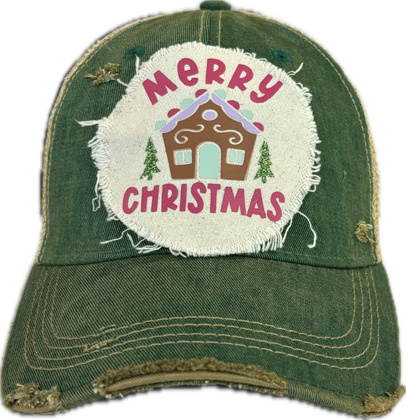Gingerbread House hat by BohoGroove with pink Merry Christmas lettering, a gingerbread house graphic, and green trees on a distressed off-white patch on a green vintage distressed snapback.