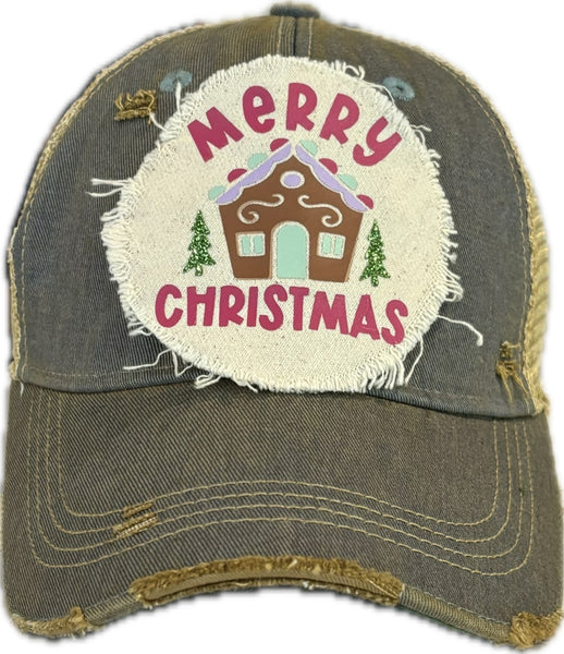 Gingerbread House hat by BohoGroove with pink Merry Christmas lettering, a gingerbread house graphic, and green trees on a distressed off-white patch on a light blue vintage distressed snapback.