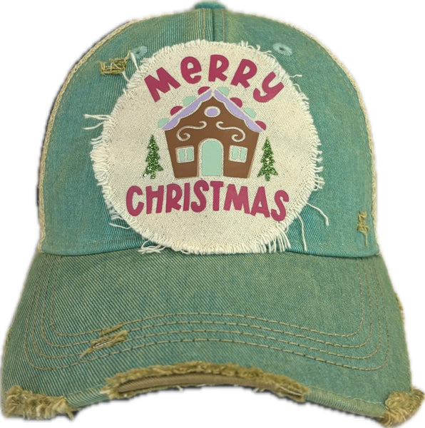Gingerbread House hat by BohoGroove with pink Merry Christmas lettering, a gingerbread house graphic, and green trees on a distressed off-white patch on an ocean blue vintage distressed snapback.