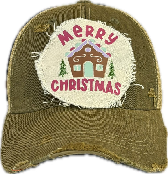 Gingerbread House hat by BohoGroove with pink Merry Christmas lettering, a gingerbread house graphic, and green trees on a distressed off-white patch on an olive vintage distressed snapback.