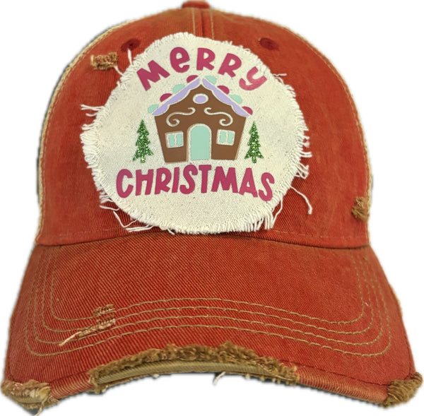 Gingerbread House hat by BohoGroove with pink Merry Christmas lettering, a gingerbread house graphic, and green trees on a distressed off-white patch on a red vintage distressed snapback.
