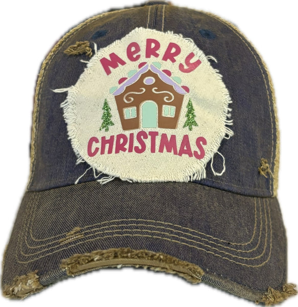 Gingerbread House hat by BohoGroove with pink Merry Christmas lettering, a gingerbread house graphic, and green trees on a distressed off-white patch on a royal blue vintage distressed snapback.
