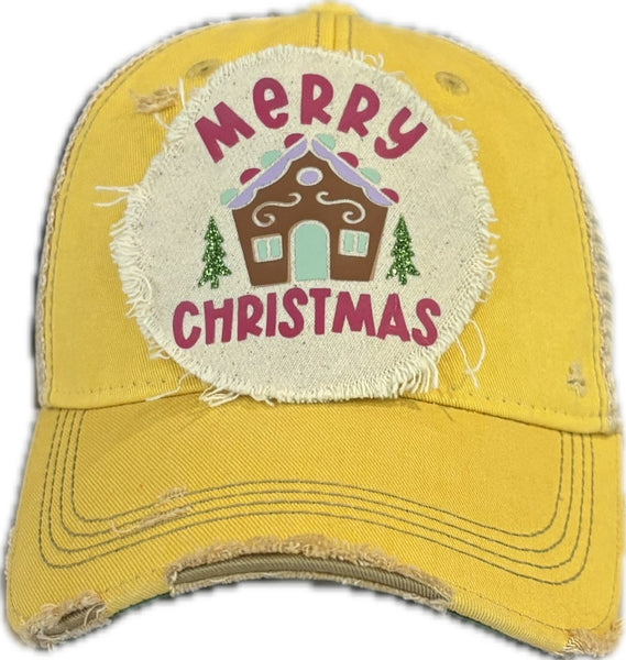 Gingerbread House hat by BohoGroove with pink Merry Christmas lettering, a gingerbread house graphic, and green trees on a distressed off-white patch on a yellow vintage distressed snapback.