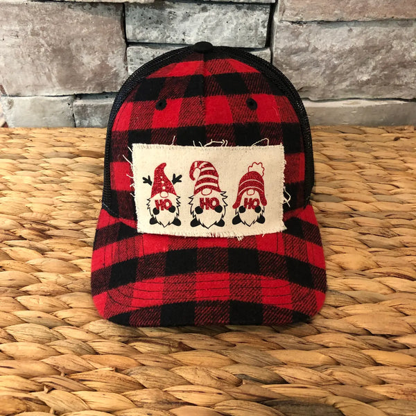 Gnome Ho Ho Ho hat by BohoGroove with three Christmas gnomes wearing red glitter hats and Ho Ho Ho lettering on a distressed off-white patch on a red and black buffalo plaid snapback trucker hat.