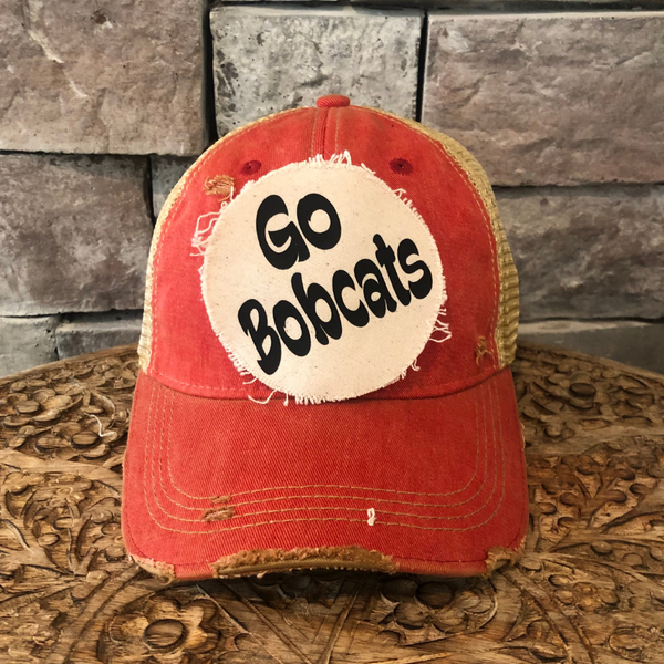 Go Bobcats hat by BohoGroove featuring black Go Bobcats lettering on a round cream frayed patch on a red vintage distressed snapback trucker hat.