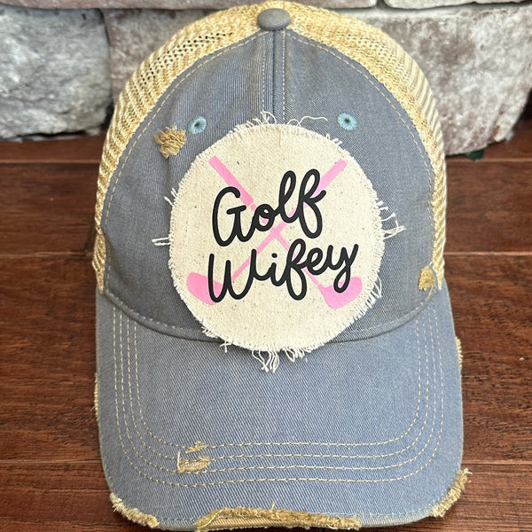 Golf Wifey hat by BohoGroove featuring black Golf Wifey lettering and pink crossed golf clubs on a light blue vintage distressed snapback hat