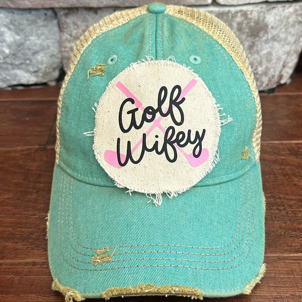 Golf Wifey hat by BohoGroove featuring black Golf Wifey lettering and pink crossed golf clubs on an ocean blue vintage distressed snapback hat