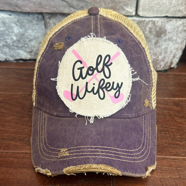 Golf Wifey hat by BohoGroove featuring black Golf Wifey lettering and pink crossed golf clubs on a purple vintage distressed snapback hat