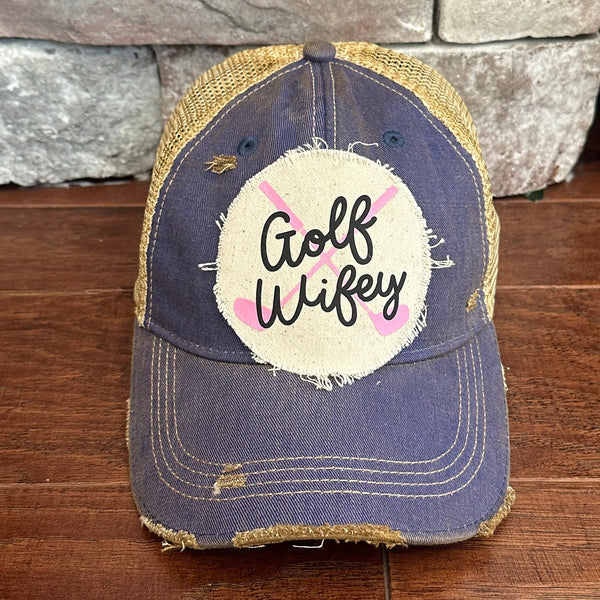 Golf Wifey hat by BohoGroove featuring black Golf Wifey lettering and pink crossed golf clubs on a royal blue vintage distressed snapback hat