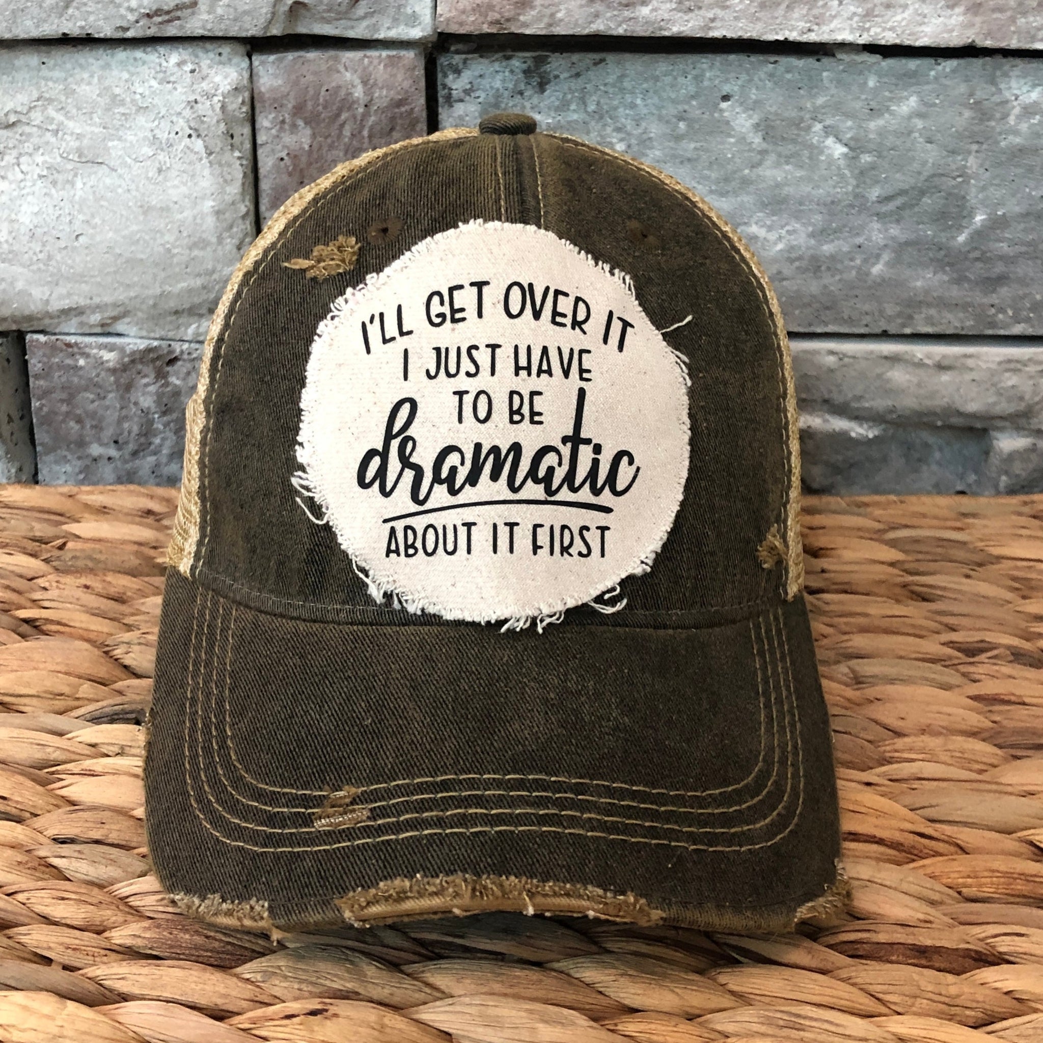 Distressed brown cap with a white patch featuring dramatic text placed on a woven surface with a stone wall background.