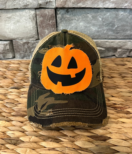 Jack-o’-Lantern hat by BohoGroove with orange pumpkin face design on a camo vintage distressed snapback trucker hat.