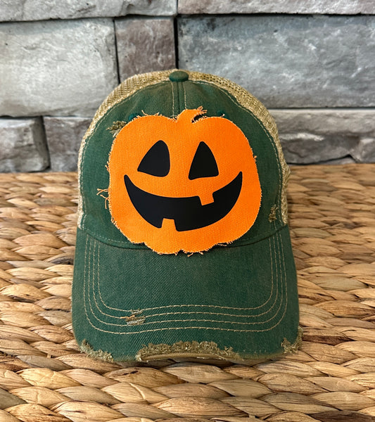 Jack-o’-Lantern hat by BohoGroove with orange pumpkin face design on a green vintage distressed snapback trucker hat.