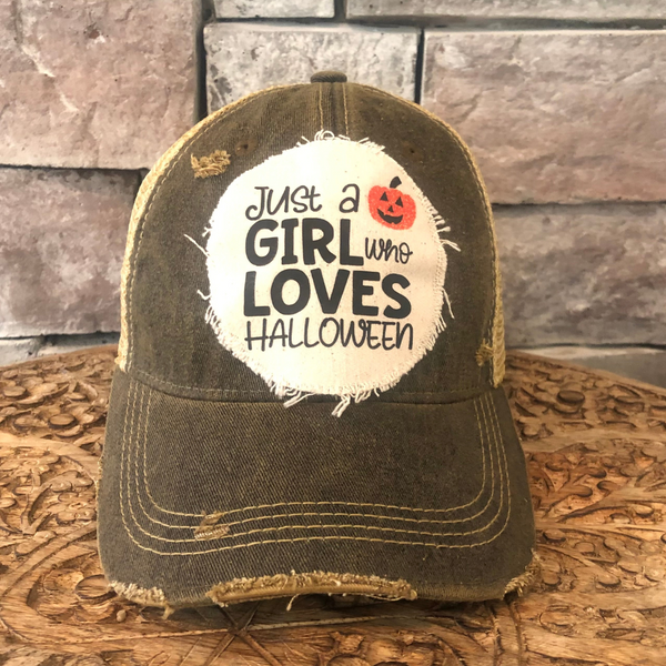 Just a Girl Who Loves Halloween hat by BohoGroove with black wording and a jack-o'-lantern graphic on a distressed off-white patch on a black vintage distressed snapback trucker hat.
