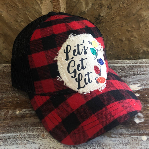Left side view of the Let's Get Lit hat by BohoGroove featuring black Let's Get Lit lettering and multicolor glitter Christmas light graphics on a distressed off-white patch on a red and black buffalo plaid snapback trucker hat with black mesh back.