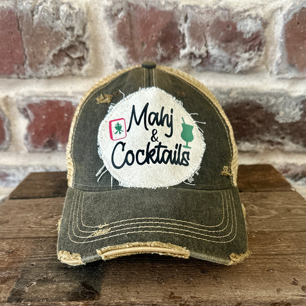 Mahj & Cocktails hat by BohoGroove featuring black Mahj & Cocktails lettering with a green cocktail graphic and Mahjong tile graphic on an off-white distressed patch on a black vintage distressed snapback trucker hat.