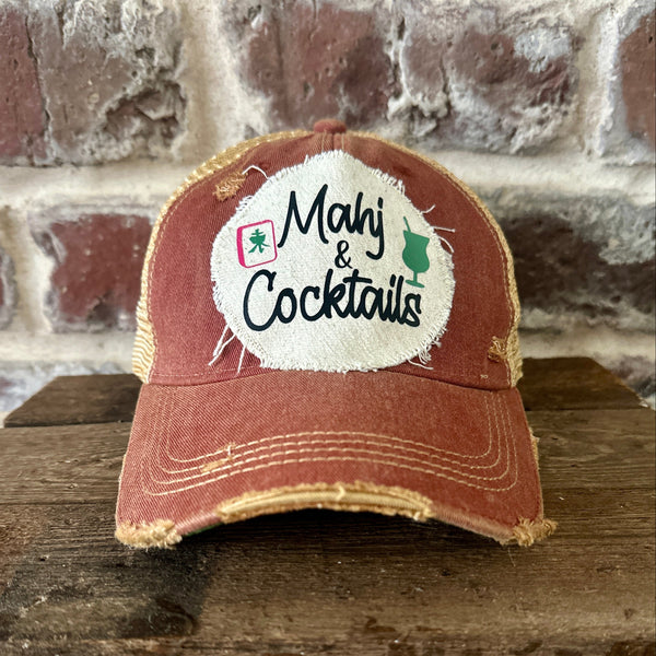Mahj & Cocktails hat by BohoGroove featuring black Mahj & Cocktails lettering with a green cocktail graphic and Mahjong tile graphic on an off-white distressed patch on a brick red vintage distressed snapback trucker hat.