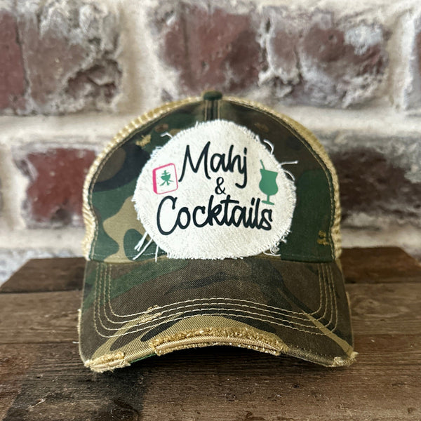 Mahj & Cocktails hat by BohoGroove featuring black Mahj & Cocktails lettering with a green cocktail graphic and Mahjong tile graphic on an off-white distressed patch on a camo vintage distressed snapback trucker hat.