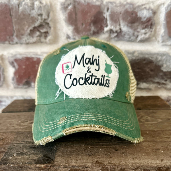Mahj & Cocktails hat by BohoGroove featuring black Mahj & Cocktails lettering with a green cocktail graphic and Mahjong tile graphic on an off-white distressed patch on a green vintage distressed snapback trucker hat.