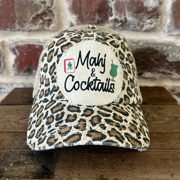 Mahj & Cocktails hat by BohoGroove featuring black Mahj & Cocktails lettering with a green cocktail graphic and Mahjong tile graphic on an off-white distressed patch on a leopard vintage distressed snapback trucker hat.