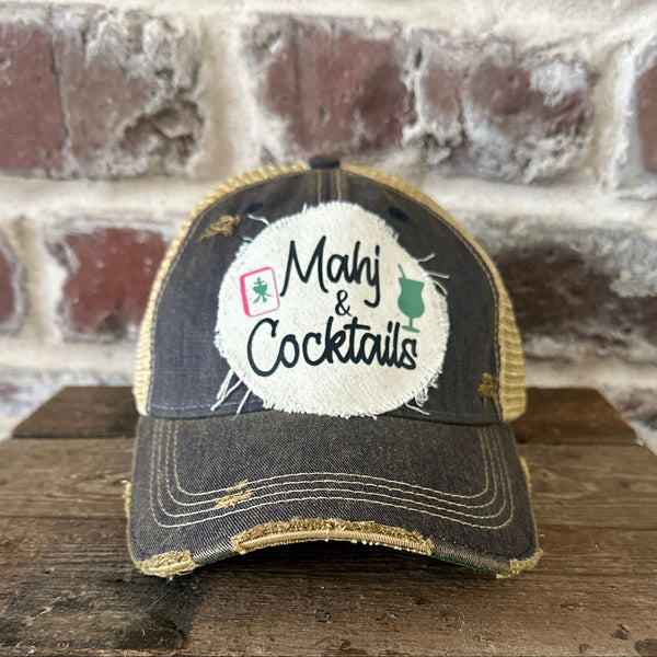 Mahj & Cocktails hat by BohoGroove featuring black Mahj & Cocktails lettering with a green cocktail graphic and Mahjong tile graphic on an off-white distressed patch on a navy vintage distressed snapback trucker hat.