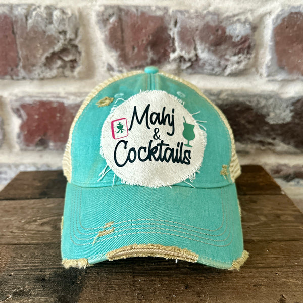 Mahj & Cocktails hat by BohoGroove featuring black Mahj & Cocktails lettering with a green cocktail graphic and Mahjong tile graphic on an off-white distressed patch on an ocean blue vintage distressed snapback trucker hat.